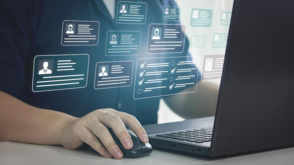 Ein Mensch arbeitet an einem Computer. Es sind Personenakten eingeblendet. 