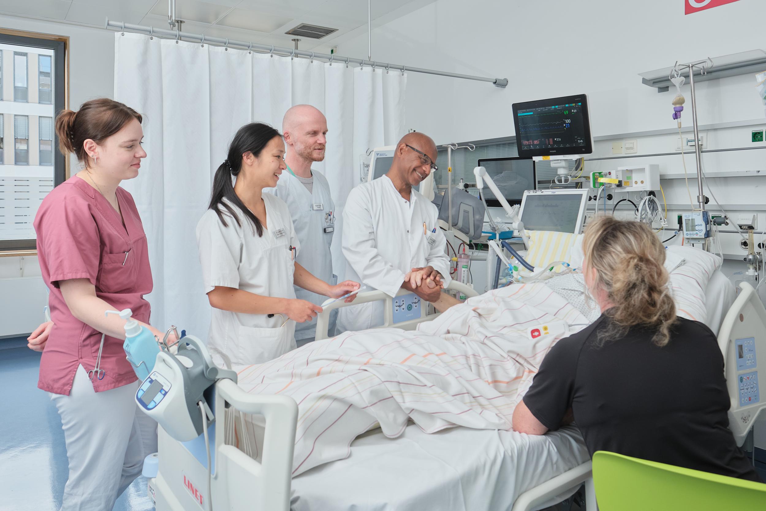 Eine Angehörige und ein medizinisches Team am Bett eines Kranken auf der Intensivstation. 