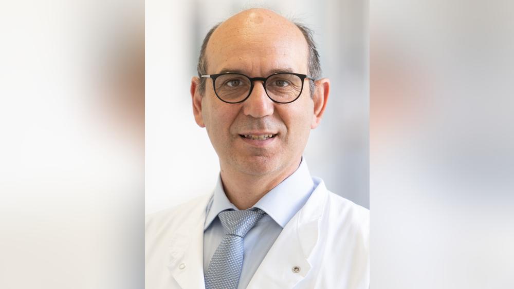 Auf dem Bild steht Prof. Christos Moustakis neben einem anderen Mann, der in eine Mappe sieht. Der Professor lächelt in die Kamera.